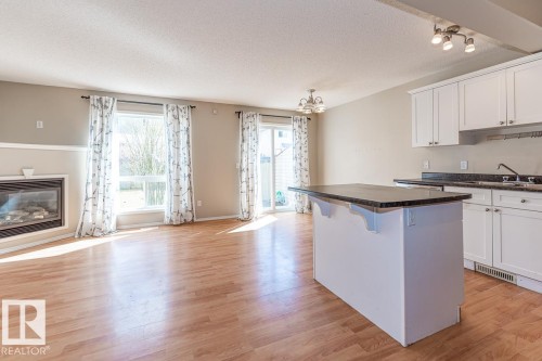 Open-concept living space with wood-finish flooring, a built-in fireplace, and a kitchen island with dark stone-finish countertop - 39 Vega Avenue, Spruce Grove, AB - Indoor Photo Showing Other Room With Fireplace