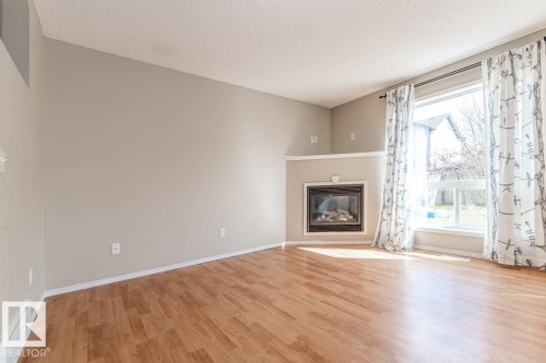 Spacious room featuring wood-finish flooring, a large window, and an inset fireplace with a mantel - 39 Vega Avenue, Spruce Grove, AB - Indoor Photo Showing Living Room With Fireplace