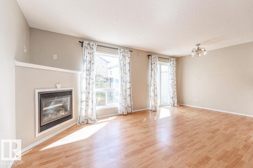 Expansive room featuring wood-finish flooring, a built-in fireplace with a white mantel, dual large windows, a sliding glass door, and a multi-bulb ceiling fixture - 39 Vega Avenue, Spruce Grove, AB - Indoor Photo Showing Living Room With Fireplace