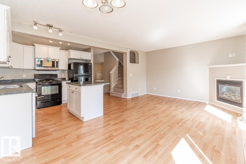 Open-concept living space featuring wood-finish flooring, a contemporary fireplace, and a kitchen with white cabinetry - 39 Vega Avenue, Spruce Grove, AB - Indoor Photo Showing Kitchen With Fireplace