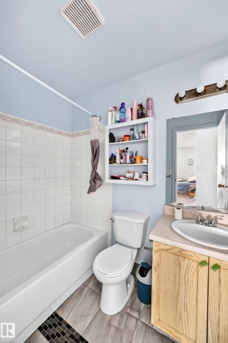 Bathroom featuring a white tub, white tiled surround, wood-finish flooring, and a vanity with a drop-in sink - #208 9619 174 St Nw, Edmonton, AB 