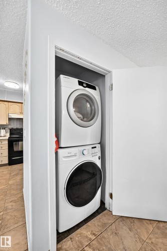 Dedicated laundry closet featuring a stackable washer and dryer, tile flooring, and a solid core door - #208 9619 174 St Nw, Edmonton, AB 