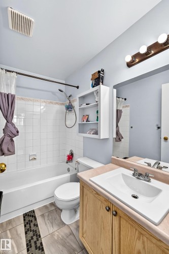 Bathroom featuring a wood-finish vanity with an integrated white sink, white tiled shower and tub combination, and light gray wall paint - #208 9619 174 St Nw, Edmonton, AB 