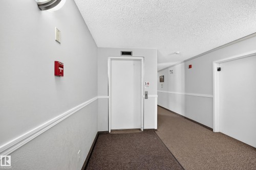 Building corridor featuring light gray walls, white trim, textured ceiling, a carpeted floor, and white doors - #208 9619 174 St Nw, Edmonton, AB 