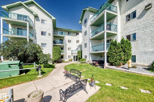 Multi-story building exterior featuring light-colored stucco, multiple balconies with turquoise railings, and varied landscaping - #208 9619 174 St Nw, Edmonton, AB 