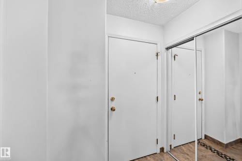 Entryway featuring a white door with brass hardware, mirrored sliding closet doors, and wood-finish flooring with a decorative tile inlay - #208 9619 174 St Nw, Edmonton, AB 