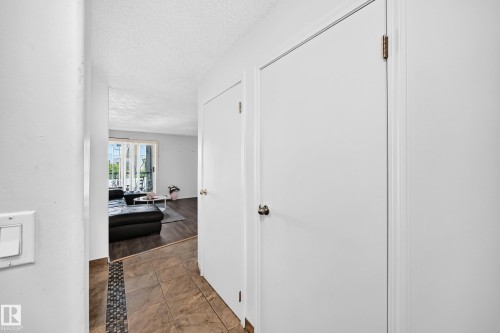 Foyer with tile flooring featuring a mosaic accent strip, leading to a living area with wood-finish flooring and a sliding glass door - #208 9619 174 St Nw, Edmonton, AB 