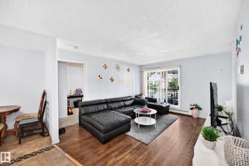 Living area with wood-finish flooring, light-toned walls, and a sliding glass door leading to an exterior space - #208 9619 174 St Nw, Edmonton, AB 