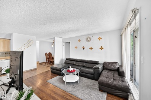 Living area featuring wood-finish flooring, white walls, and a large window with vertical blinds - #208 9619 174 St Nw, Edmonton, AB 