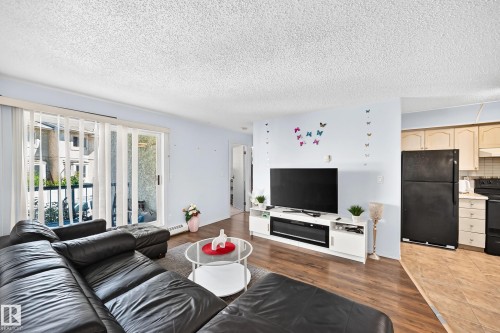 Living area featuring wood-finish flooring and direct access to a private balcony through sliding glass doors - #208 9619 174 St Nw, Edmonton, AB 