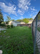 Expansive grassy yard area featuring a detached garage with siding exterior, a wood privacy fence, and chain-link fencing - 