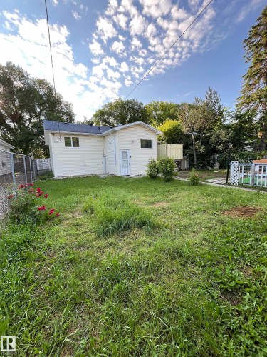 Expansive backyard featuring a partial chain-link fence, a white vinyl-sided exterior, a white storm door, and an upper-level wood deck - 11938 70 Nw, Edmonton, AB 