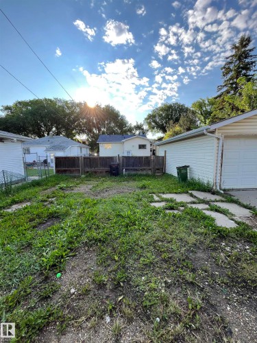 Spacious backyard featuring a wood fence, concrete patio stones, and a detached garage with vinyl siding and a white garage door - 11938 70 Nw, Edmonton, AB 