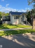 Light yellow siding exterior with a dark shingle roof, front entry steps, a screened-in side porch, and a sidewalk - 