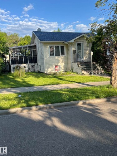 Charming single-story residence with light-colored siding, a dark shingle roof, and a screened-in porch with lattice detailing - 11938 70 Nw, Edmonton, AB 