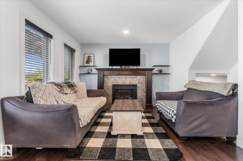 Living area featuring wood-finish flooring and a tiled fireplace with a dark wood mantel and floating shelves - 6 Sedona Place, Fort Saskatchewan, AB - Indoor Photo Showing Living Room With Fireplace