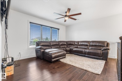 Spacious room featuring rich wood-finish flooring, a large window with horizontal blinds, and a contemporary ceiling fan with integrated lighting - 6 Sedona Place, Fort Saskatchewan, AB - Indoor Photo Showing Living Room