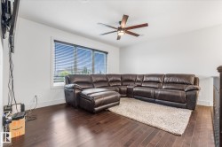 Spacious room featuring rich wood-finish flooring, a large window with horizontal blinds, and a contemporary ceiling fan with integrated lighting - 