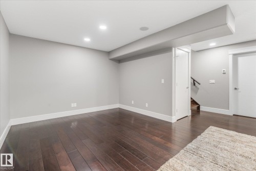 Spacious room featuring dark wood-finish flooring, light grey painted walls, white trim, recessed ceiling lighting, and a visible stairwell with a dark wood handrail - 6 Sedona Place, Fort Saskatchewan, AB - Indoor