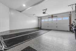 Spacious garage featuring a finished epoxy floor, white paneled garage door with windows, automatic garage door opener, and recessed ceiling lighting - 