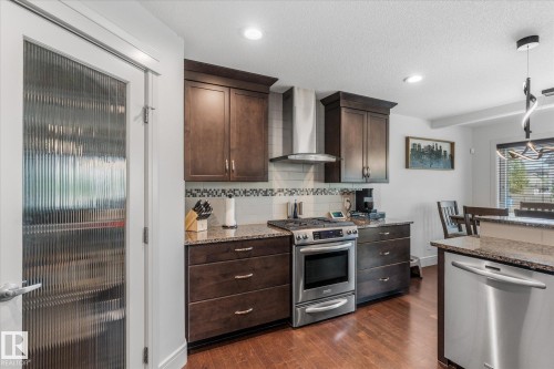 Kitchen featuring dark wood cabinetry, granite countertops, stainless steel appliances, a tile backsplash, and wood-finish flooring - 6 Sedona Place, Fort Saskatchewan, AB - Indoor Photo Showing Kitchen With Stainless Steel Kitchen With Upgraded Kitchen