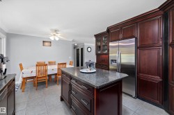 Kitchen featuring dark wood cabinetry, a central island with a stone-finish countertop, a stainless steel refrigerator, and recessed lighting - 