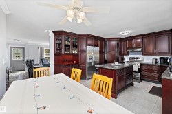 Kitchen featuring rich wood cabinetry, stainless steel appliances, a center island with a stone-finish countertop, tile flooring, and recessed lighting - 