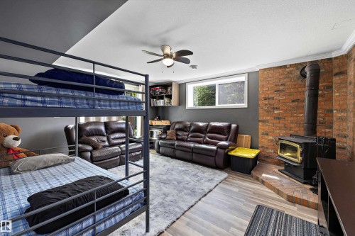 Spacious room featuring wood-finish flooring, a prominent brick accent wall, and a corner wood-burning stove with a tiled hearth - 53257 Rge Road 211, Rural Strathcona County, AB - Indoor With Fireplace