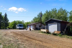 Gravel driveway with two detached structures featuring composition shingle roofs and multiple garage doors - 