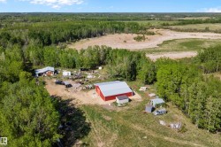 Expansive rural property featuring a large red barn with a silver roof, multiple outbuildings, and a cleared building site - 