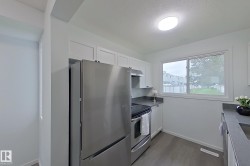 Kitchen featuring stainless steel appliances, white cabinetry, dark countertops, and wood-finish flooring - 