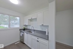 Kitchenette featuring white cabinetry, gray countertops, a stainless steel sink, and a built-in dishwasher - 
