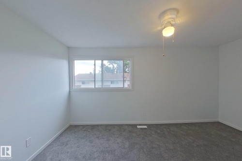 Bright room featuring a window with white trim, fresh white walls, new gray carpeting, and a ceiling fan with integrated lighting - 209 Dickinsfield Court Nw, Edmonton, AB 