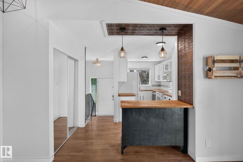 Kitchen pass-through featuring an accent wall with patterned tile, two suspended light fixtures, and a wood-finish countertop - 1071 Millbourne Road Nw, Edmonton, AB 