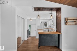 Kitchen pass-through featuring an accent wall with patterned tile, two suspended light fixtures, and a wood-finish countertop - 