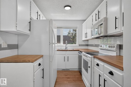Galley kitchen featuring white cabinetry with black hardware, wood-finish countertops, and a white tile backsplash - 1071 Millbourne Road Nw, Edmonton, AB 