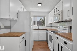 Galley kitchen featuring white cabinetry with black hardware, wood-finish countertops, and a white tile backsplash - 