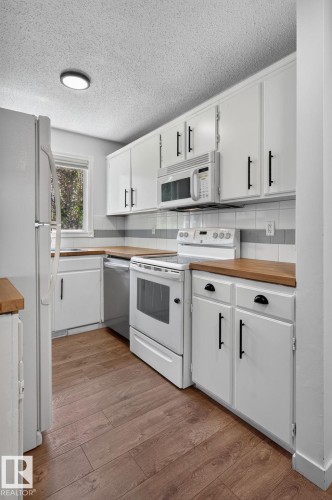 Kitchen featuring white cabinetry with black hardware, wood-finish countertops, and a white appliance suite - 1071 Millbourne Road Nw, Edmonton, AB 