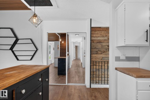 Interior featuring wood-finish flooring, white cabinetry with wood countertops, a black decorative railing, and a rustic wood accent wall - 1071 Millbourne Road Nw, Edmonton, AB 