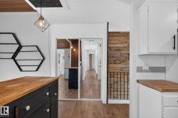 Interior featuring wood-finish flooring, white cabinetry with wood countertops, a black decorative railing, and a rustic wood accent wall - 