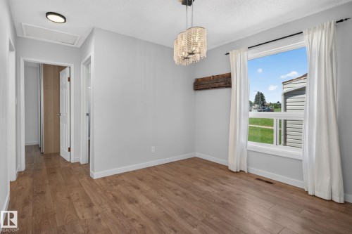 Bright interior space featuring wood-finish flooring, light grey walls, and a large window with white trim and drapes - 1071 Millbourne Road Nw, Edmonton, AB 