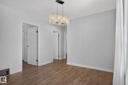 Open interior space featuring wood-finish flooring, a contemporary chandelier, multiple paneled doors, and light-toned wall finishes - 