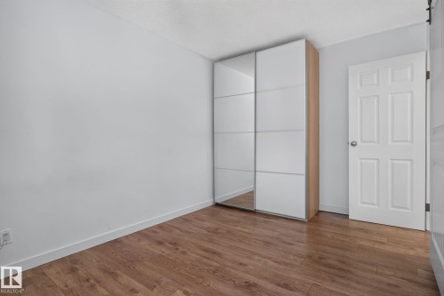 Room featuring wood-finish flooring, light grey walls, and a built-in wardrobe with mirrored and white panel sliding doors - 1071 Millbourne Road Nw, Edmonton, AB 