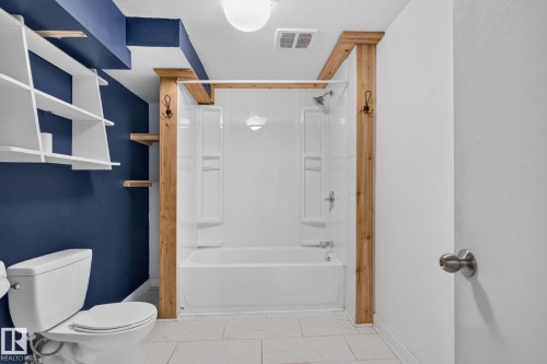 Full bathroom featuring a white tub/shower combination, white toilet, and light-toned tile flooring - 1071 Millbourne Road Nw, Edmonton, AB 