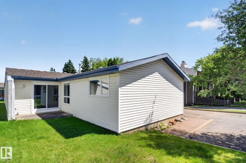 Rear exterior featuring light-toned siding, a glass sliding door, and a small patio area - 1071 Millbourne Road Nw, Edmonton, AB 
