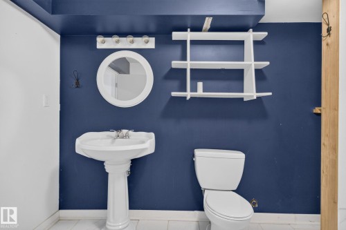 Bathroom featuring a white pedestal sink, circular mirror, and wall-mounted vanity lighting - 1071 Millbourne Road Nw, Edmonton, AB 