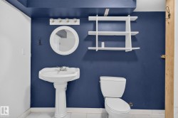 Bathroom featuring a white pedestal sink, circular mirror, and wall-mounted vanity lighting - 