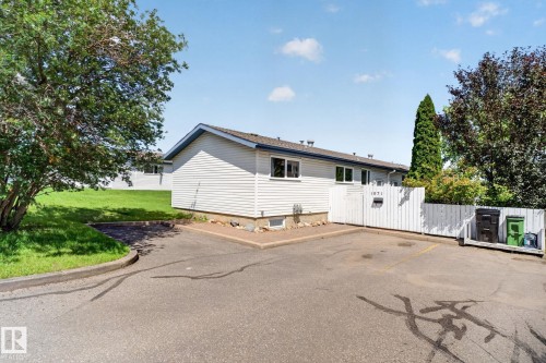 Exterior view featuring light-colored horizontal siding, a white privacy fence, and multiple mature trees - 1071 Millbourne Road Nw, Edmonton, AB 