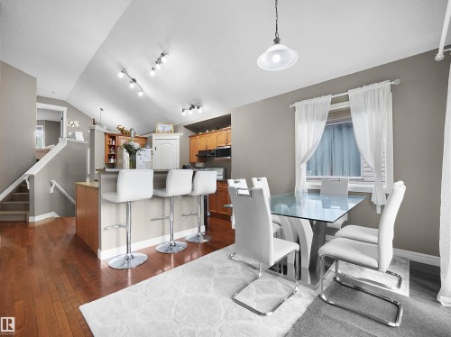 Open-concept living area featuring a vaulted ceiling with track lighting, hardwood flooring, a breakfast bar, and a dining area with a pendant light fixture - 4021 158 Avenue Nw, Edmonton, AB - Indoor Photo Showing Dining Room