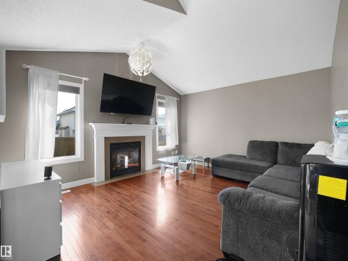 Living area featuring vaulted ceilings, wood-finish flooring, a built-in fireplace with a white mantel, and multiple windows - 4021 158 Avenue Nw, Edmonton, AB - Indoor Photo Showing Living Room With Fireplace